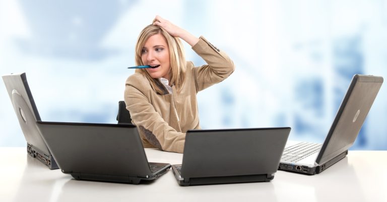 Woman looking at four laptops and scratching her head in frustration, as a data engineer fearing being left out